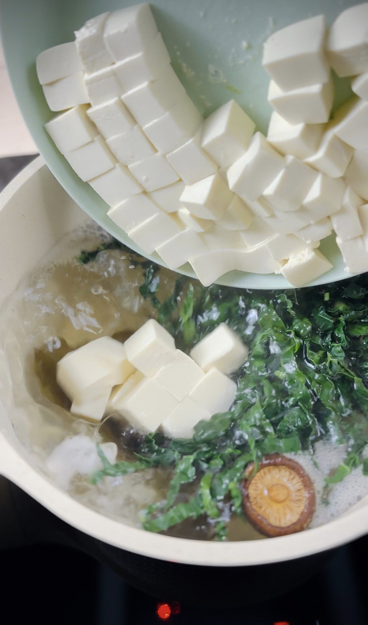 Tofu cubes being added into a saucepan full of broth on the stove.