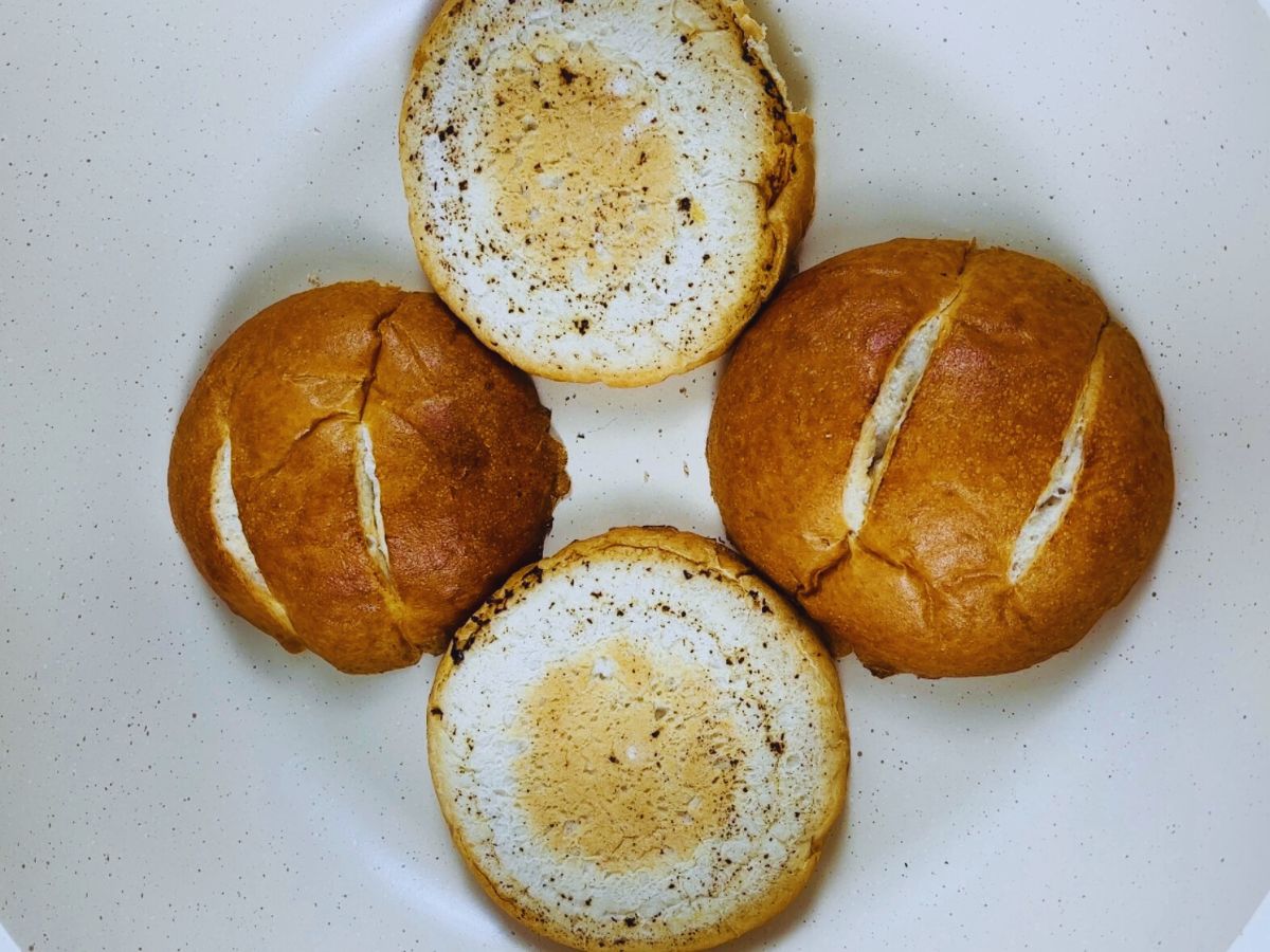 Halved buns, being toasted in a large frying pan, slightly charred and toasted.