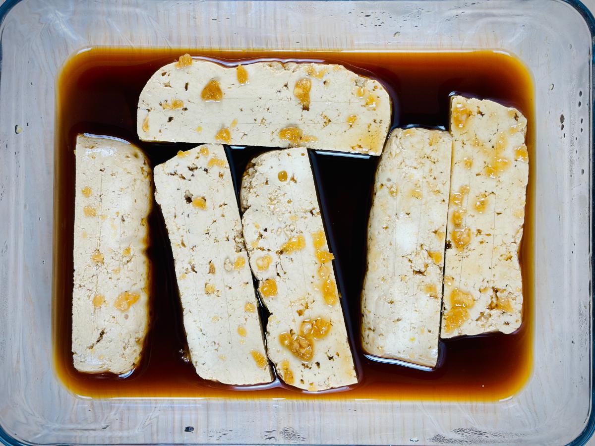 Tofu cut into large, chunky finger length pieces, soaking in teriyaki marinade, speckled with crushed garlic.