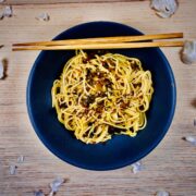 Dark pasta bowl with Japanese spaghetti topped with takana, chili and seasoning with chopsticks resting on the rim