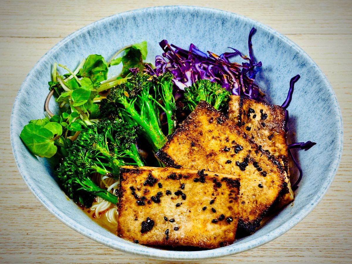 A large ramen bowl containing noodles, soup broth and topped with tofu, red cabbage and green vegetables.