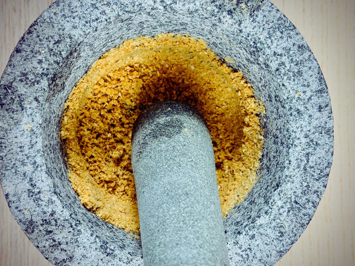 Pestle and mortar in process of crushing some light brown seeds into a fine powder.