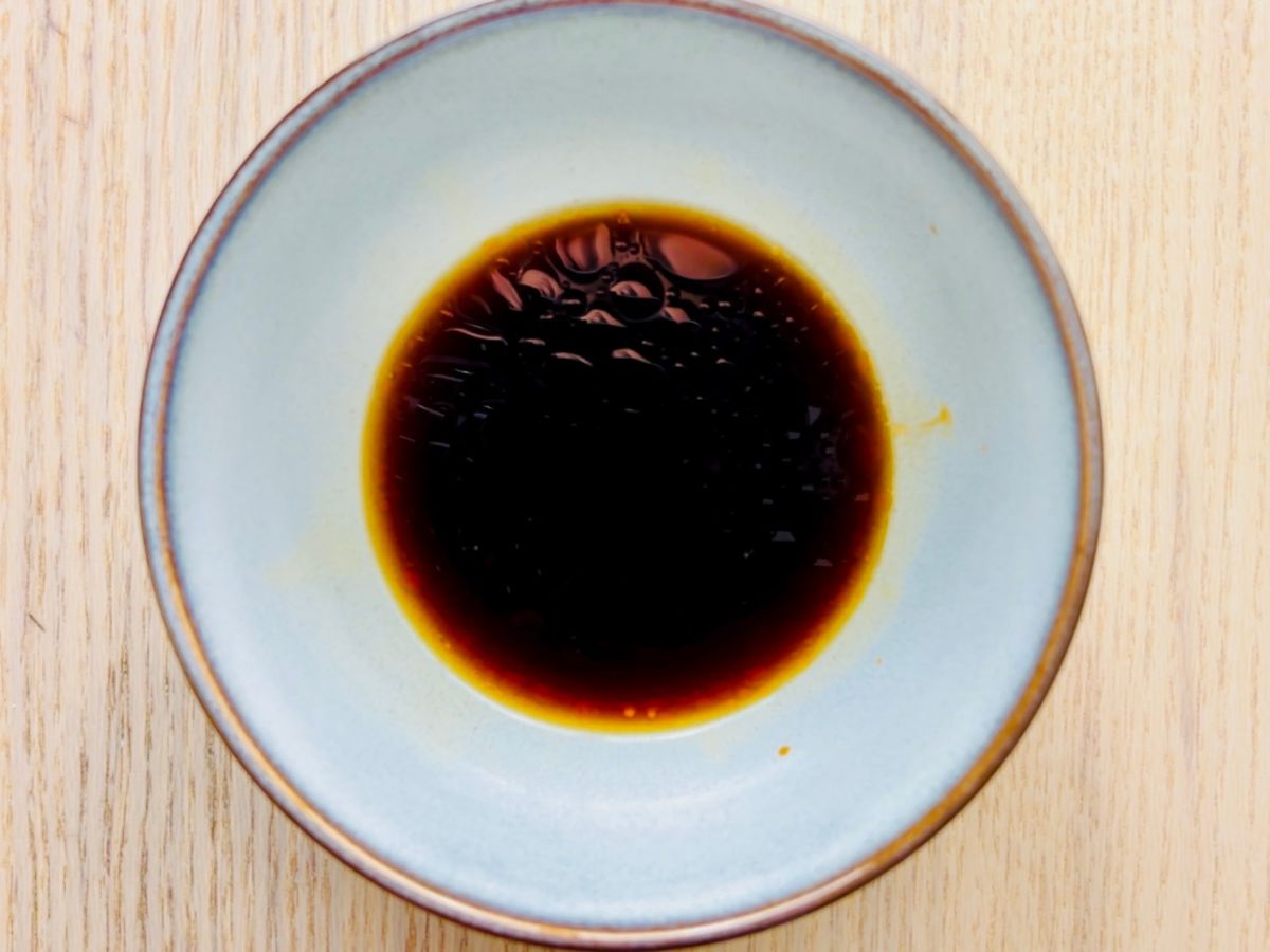 A small, shallow dish containing a black liquid with some small round spots of oil floating on the top.