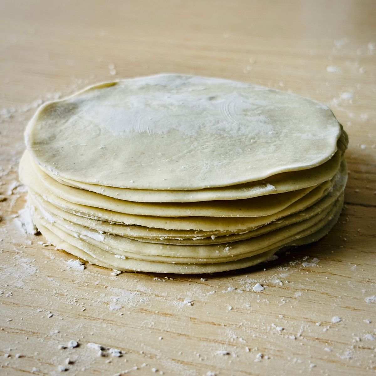 A stack of small flat rounds of dough, sat on a tabletop surface with a thin layer of white flour scattered around.