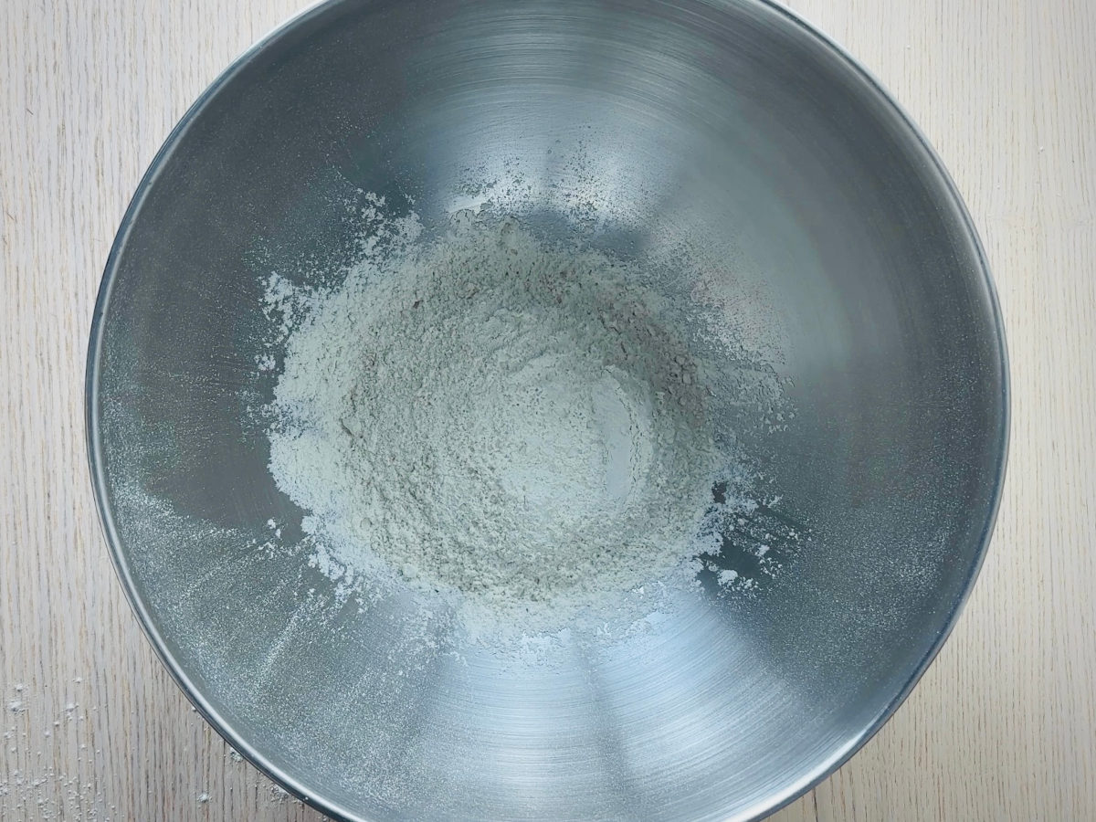 A large metal mixing bowl containing sifted white flour and a little salt.