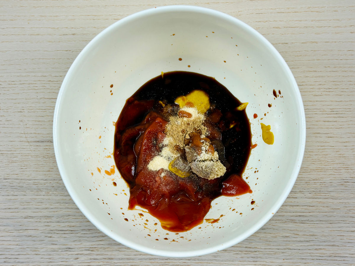 A large mixing bowl containing a splattering of different red, brown and yellow sauces and brown and white powdered seasonings to make tonkatsu sauce.