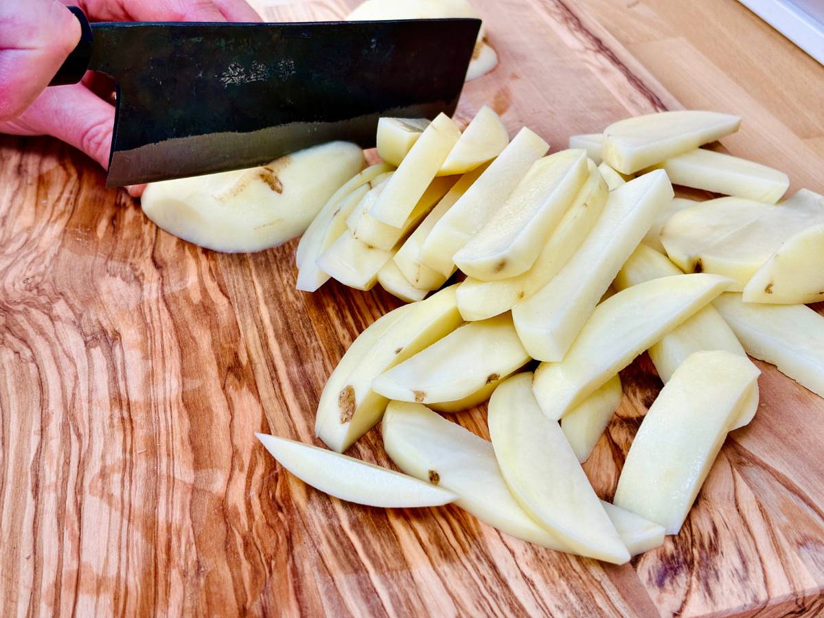 Maris Piper potatoes being sliced into even strips, approximately 1.5-2 cm thick, to make vegan Japanese togarashi fries.