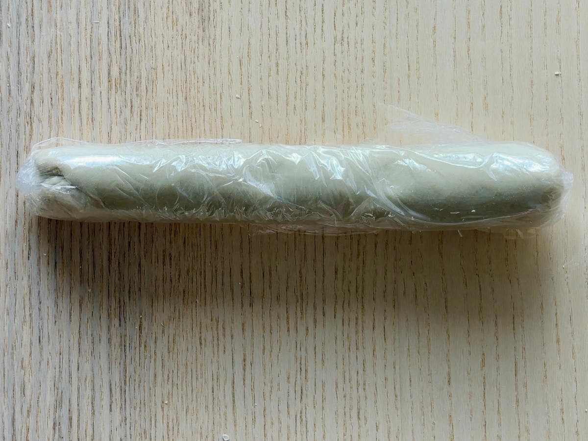 A long sausage-shaped piece of white dough resting, wrapped in cling film.