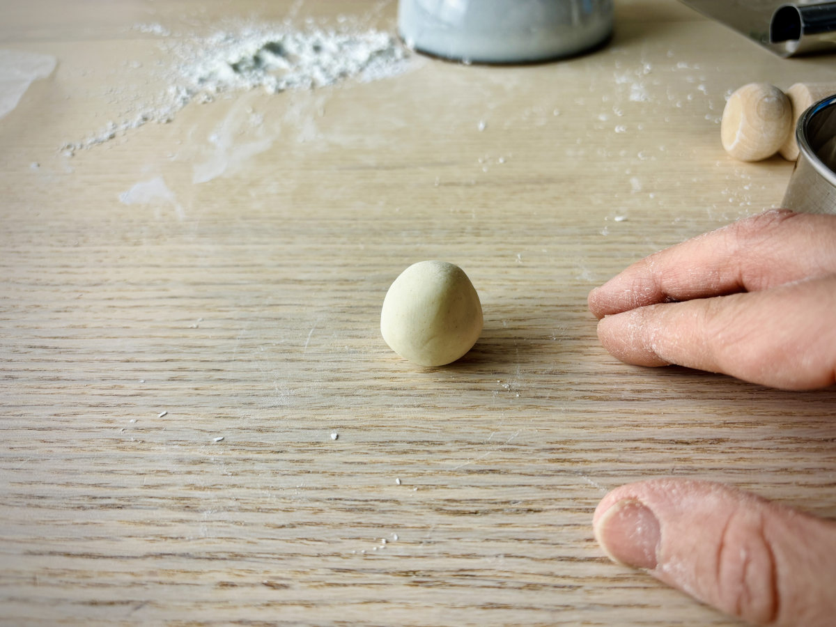 A small round ball of dough on a tabletop, ready to be rolled out into a flat circular shaped gyoza skin wrapper.