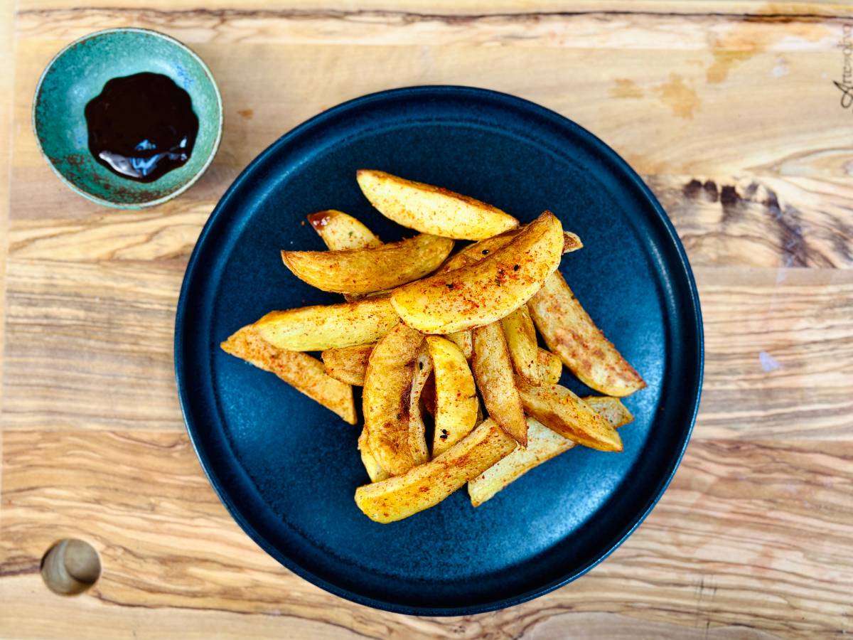 A plate of home-cooked potato fries seasoned with Japanese spices, shichimi togarashi, and served with vegan Japanese tonkatsu sauce on the side.