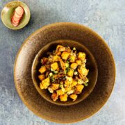 Brown ceramic bowl with crispy golden tofu, vegetables and spring onions next to pickled radish