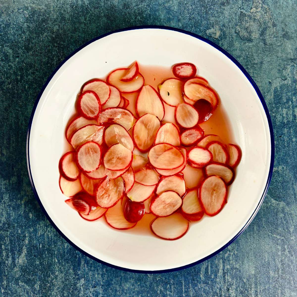 A white dish containing thinly sliced pink radish (with white flesh and pink skin), in some pink-brown coloured liquid.