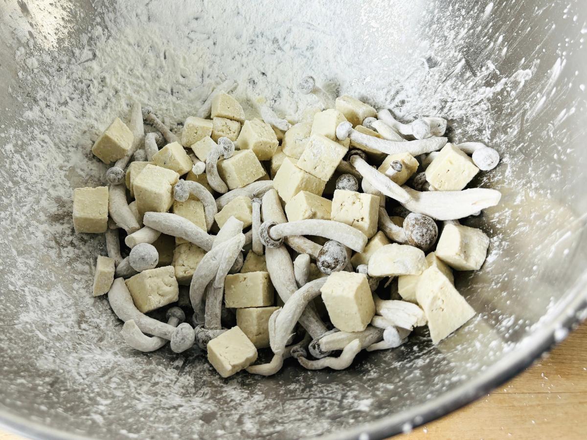 Shimeji mushrooms and cubed tofu coated in cornstarch in a bowl, ready for frying