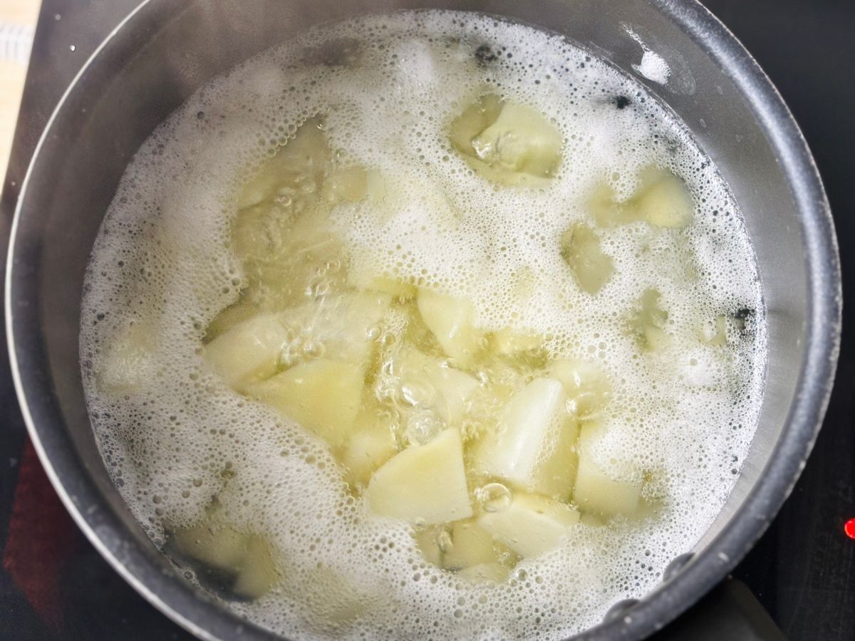 A saucepan on heat full of bubbling water and chopped white potatoes.