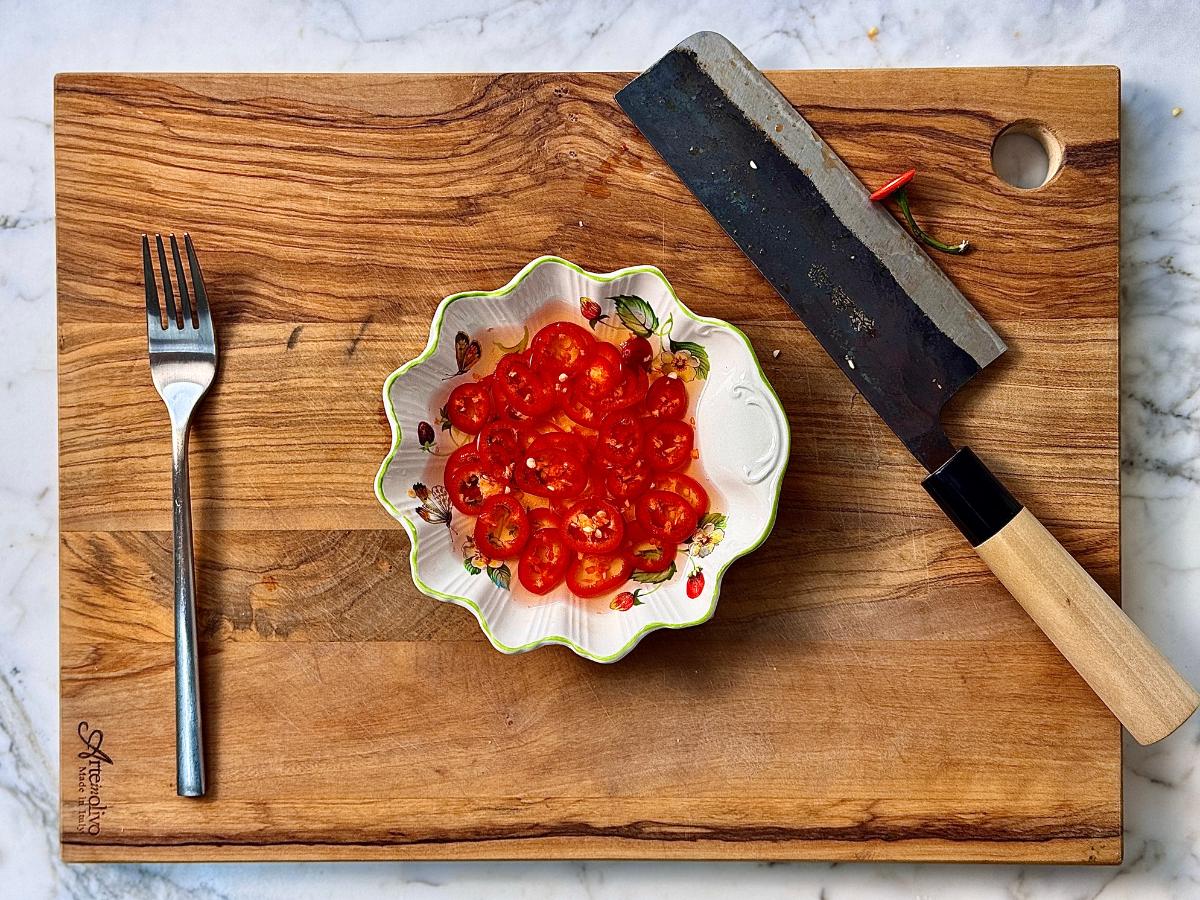 sliced red chillis on a shallow scalloped plate pickling in pickling juice