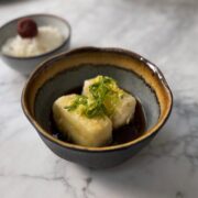 Small bowl with two cubes of crispy agedashi tofu in a dashi sauce garnished with spring onions
