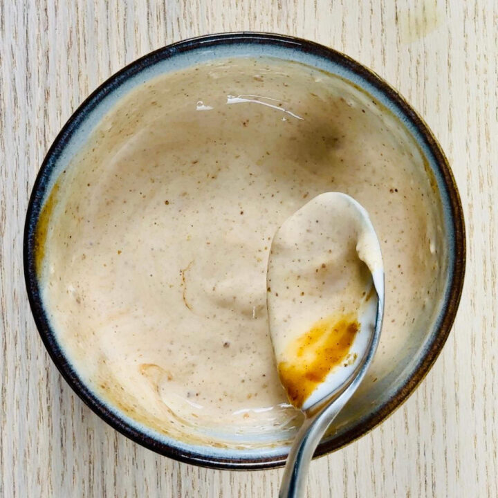 A top-down view of a small bowl filled with creamy mayo, as a spoon stirs in ground sesame seeds and rich, brown tonkatsu sauce.