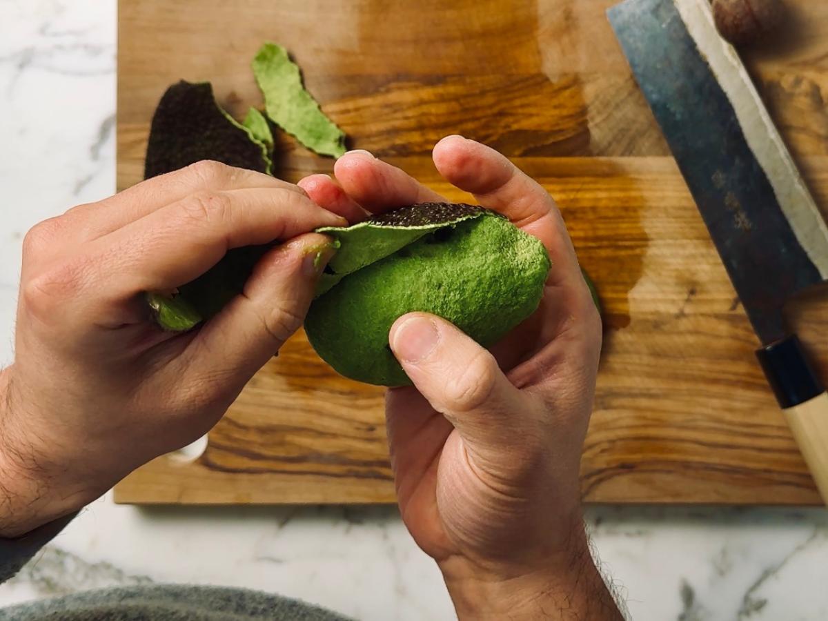 An avocado being peeled before cutting in half and removing the seed.