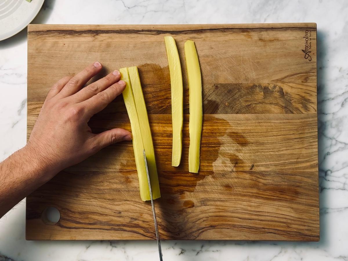 Takuan being cut into long, uniform strips roughly 10cm long and 1.5cm thick, laid out in a tidy row on a wooden chopping board.