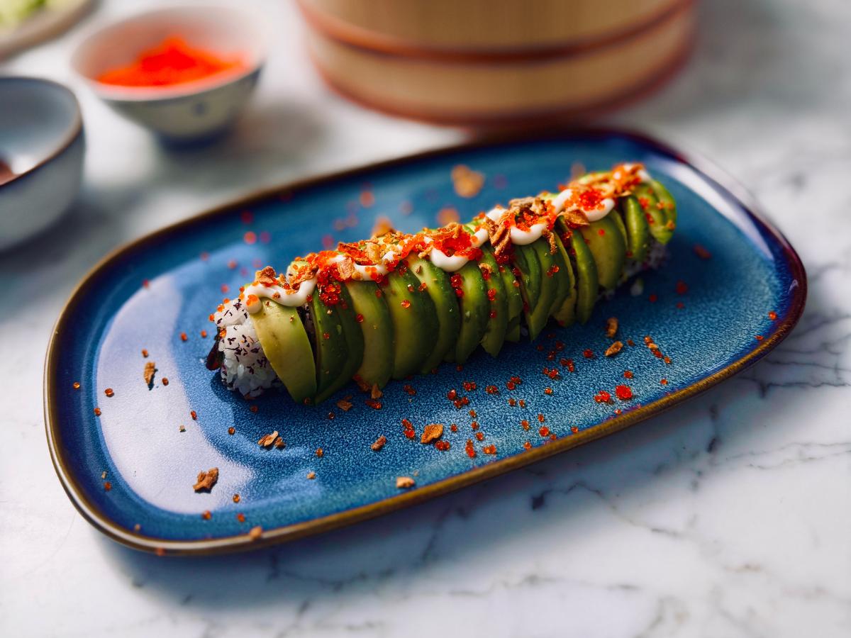 Vegan sushi roll on a serving platter topped with avocado, vegan caviar, shichimi, vegan kewpie mayo and dried onion flakes.
