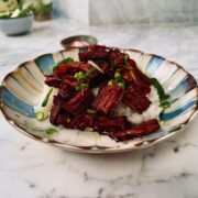 Bowl of white rice topped with tender slices of vegan Japanese beef donburi with spring onions and pak choi