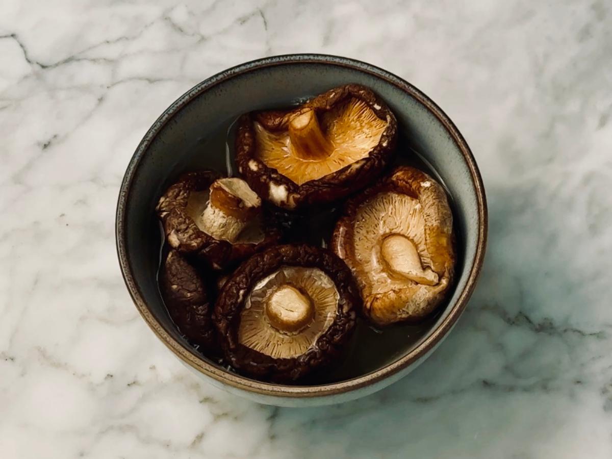 Dried shiitake mushrooms in a small bowl with hot water poured over them.
