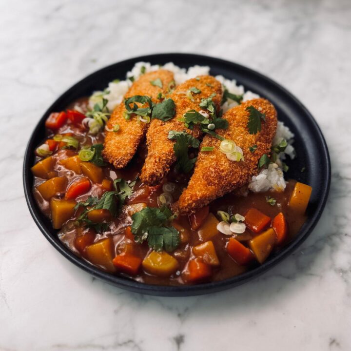 A plated serving of sweet potato katsu curry with three golden panko-crusted cutlets on top of curry-covered Japanese white rice, garnished with fresh cilantro and green onions.