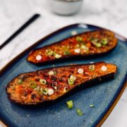 Halved miso-glazed aubergines on a serving platter garnished with spring onions, sesame seeds and aonori