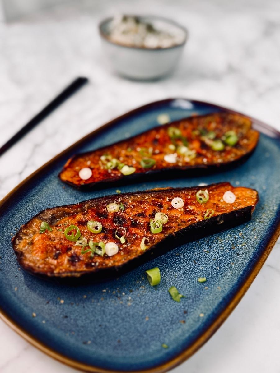 Halved miso-glazed aubergines on a serving platter, beautifully caramelised and garnished with sliced spring onions, sesame seeds, and aonori.
