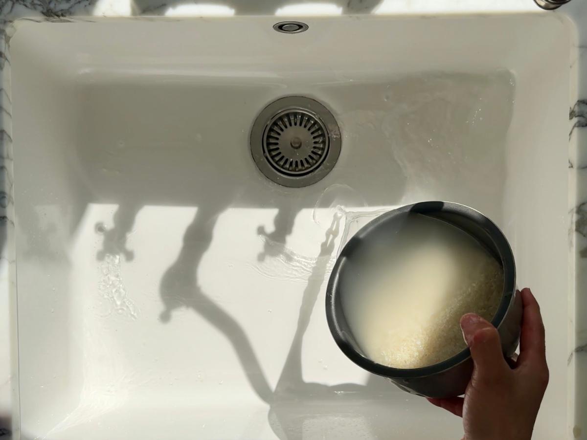 A hand rinsing Japanese short-grain rice in a bowl of water to remove excess starch.