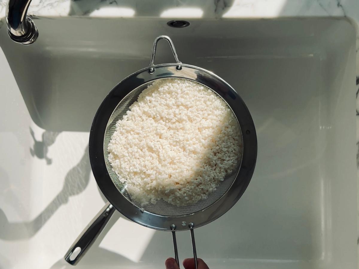 Drained rice resting in a fine mesh strainer over a sink.
