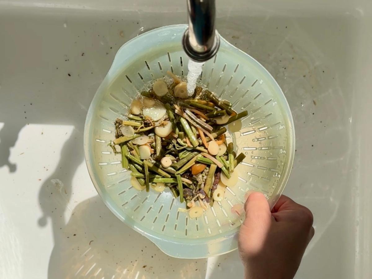 A colander filled with preserved mountain vegetables being rinsed under running water.
