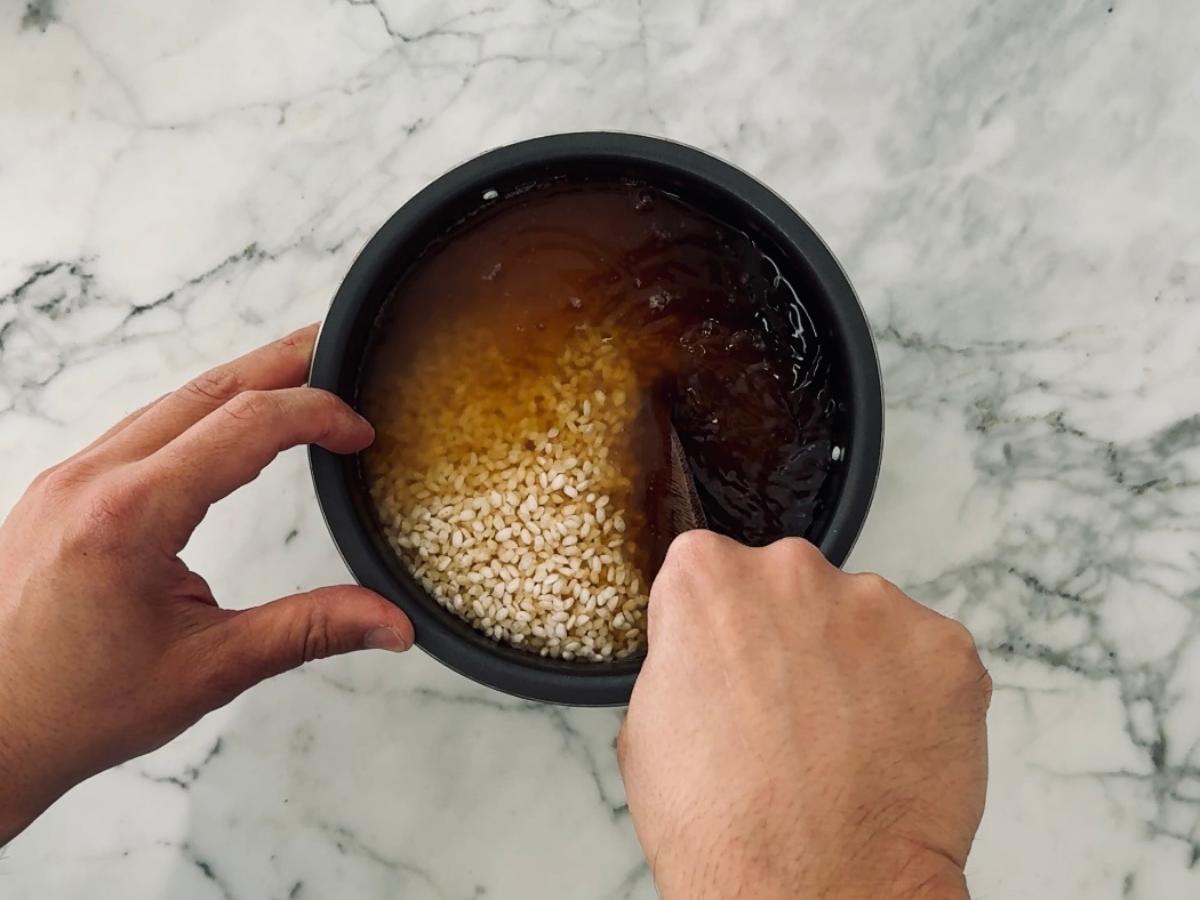 Mixing rice and seasonings together in a rice cooker bowl.
