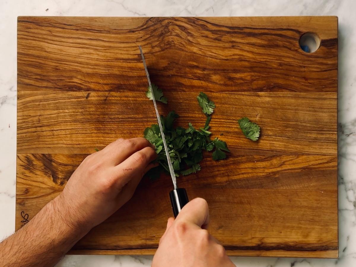 Fresh cilantro (coriander) being roughly chopped on a cutting board.
