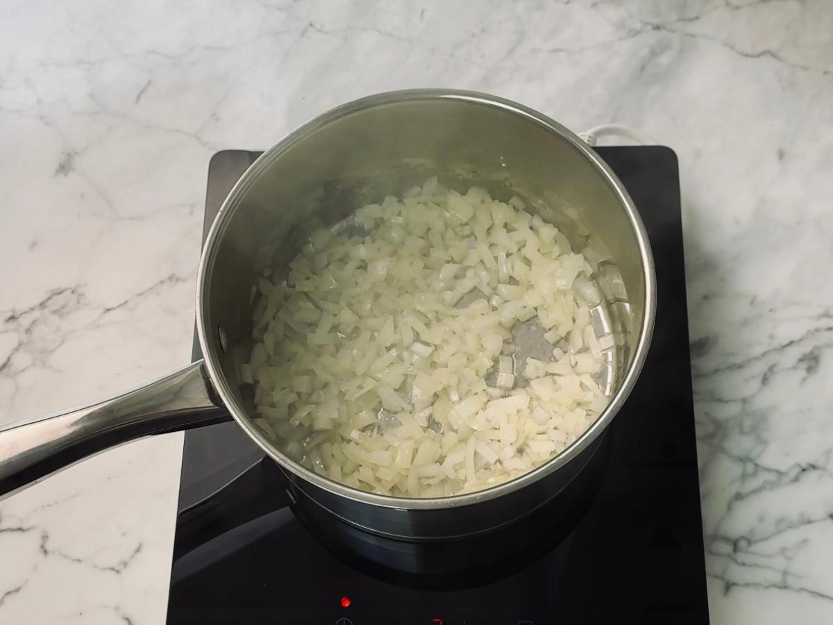 Onions frying in a saucepan with oil, beginning to soften before turning golden brown.