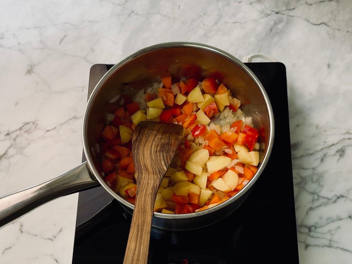 Mixed vegetables being added to the hot saucepan on the stovetop, with soy sauce and salt.
