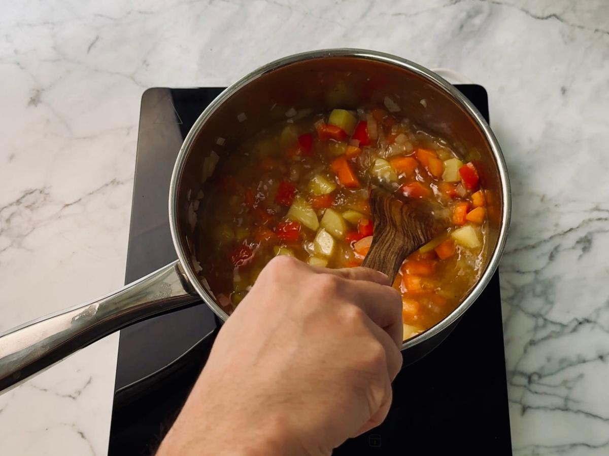 Simmering vegetables being being stirred in water, inside a large saucepan, over heat.