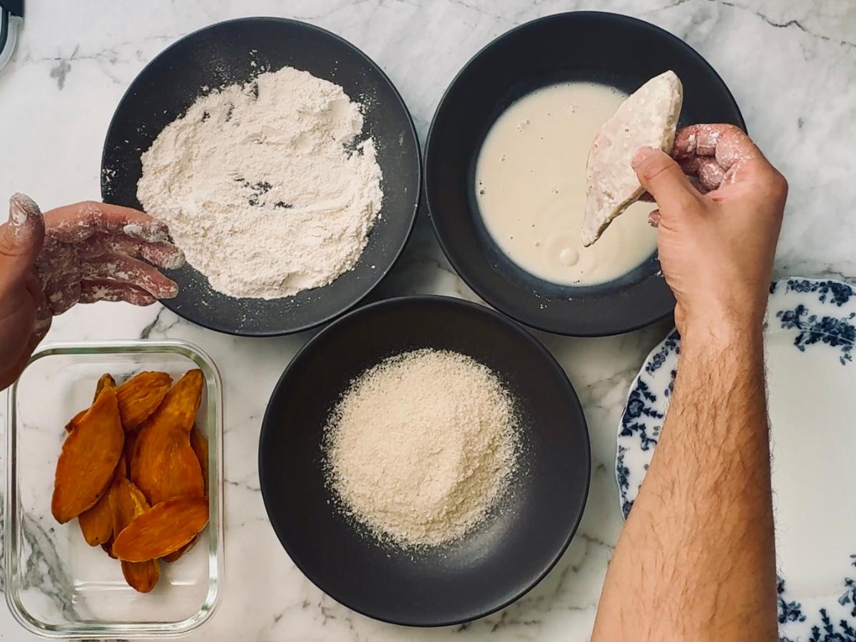 Sweet potato slices being double-dipped in flour and milk before coating with panko breadcrumbs.