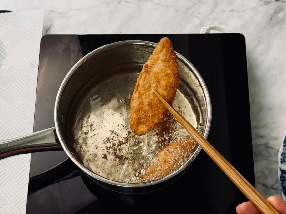 Panko-fried sweet potato 'katsu' being lifted out of a deep-frying saucepan, ready to place on a paper-lined tray to drain the excess oil.