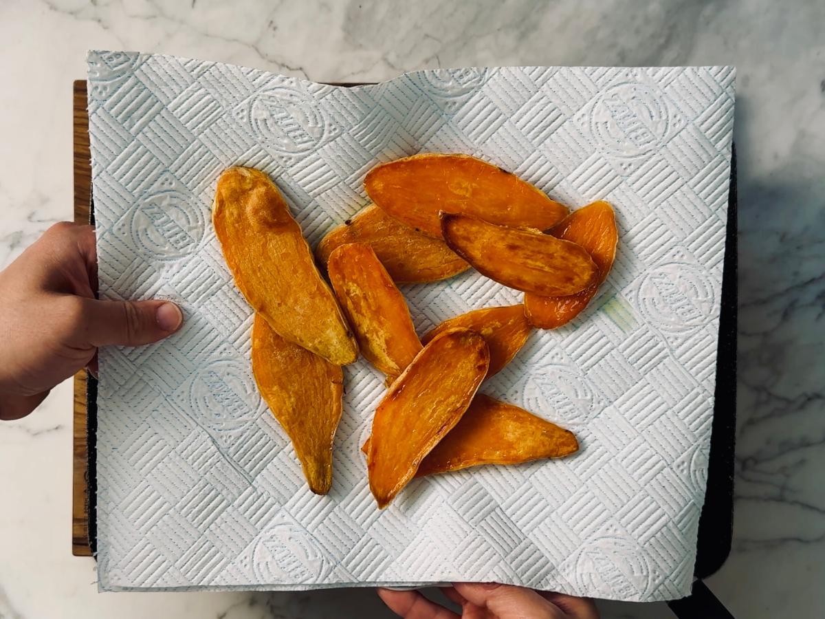 Roasted sweet potato slices cooling on a kitchen paper-lined plate to absorb excess oil.