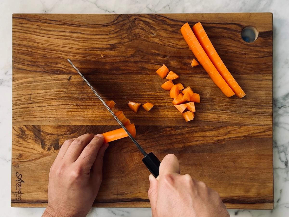 Carrot being sliced lengthwise into strips and then into small cubes.