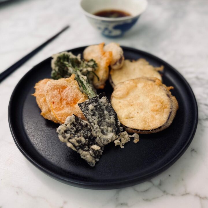 Close up view of a plate of crispy vegan vegetable tempura in front of a bowl of soy dipping sauce.