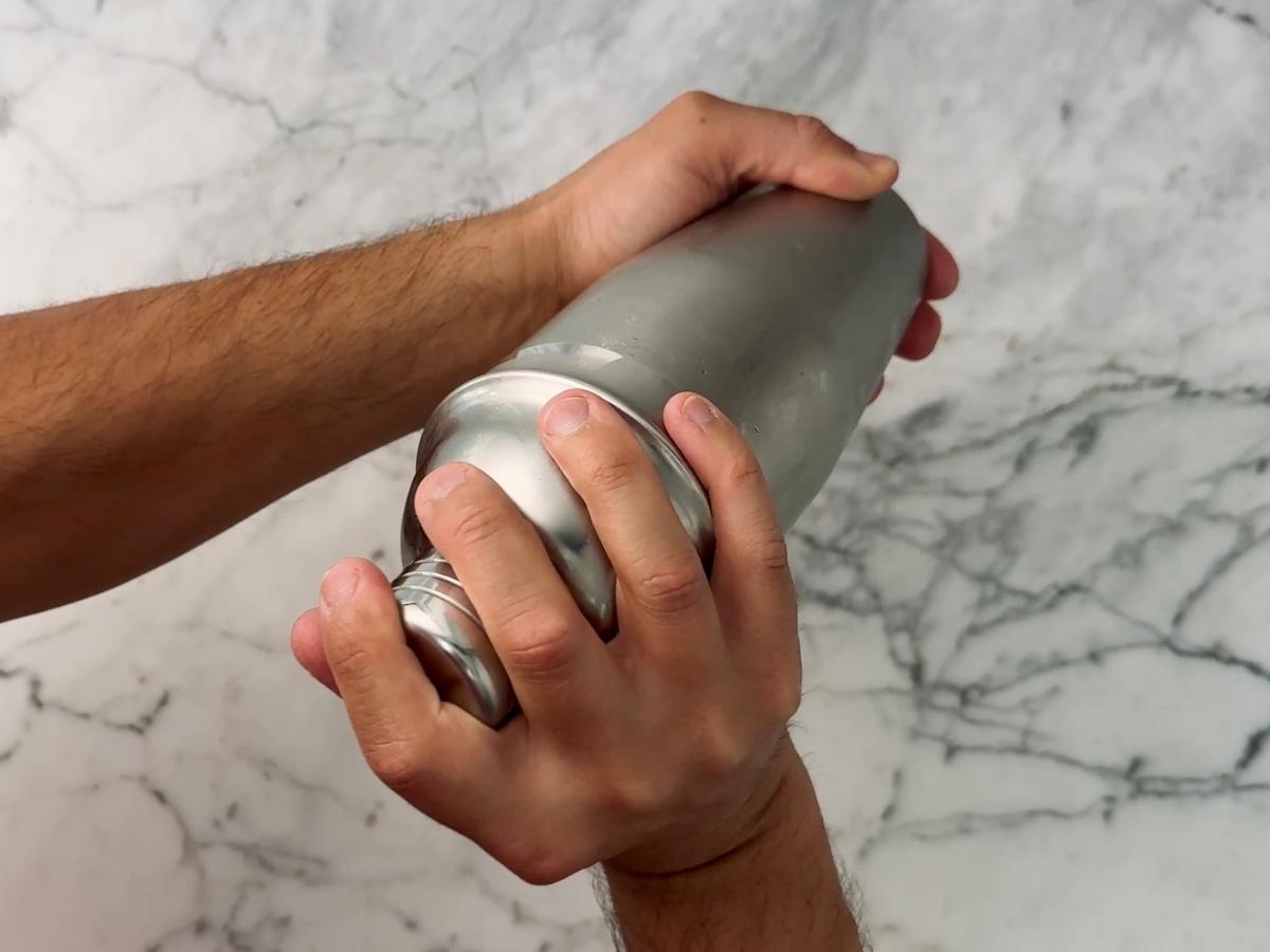 Close-up of hands shaking the sealed cocktail shaker vigorously.