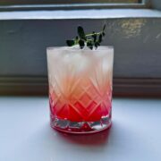 Yuzu gin fizz served in an old-fashioned glass over ice with a fresh herb garnish