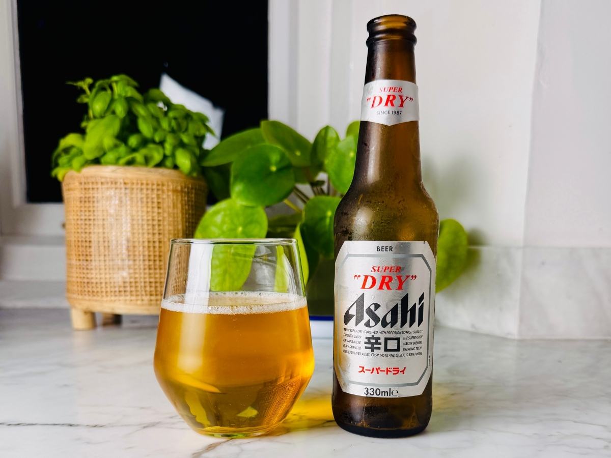 Can of Asahi Super Dry next to a glass of golden lager with a thin white head