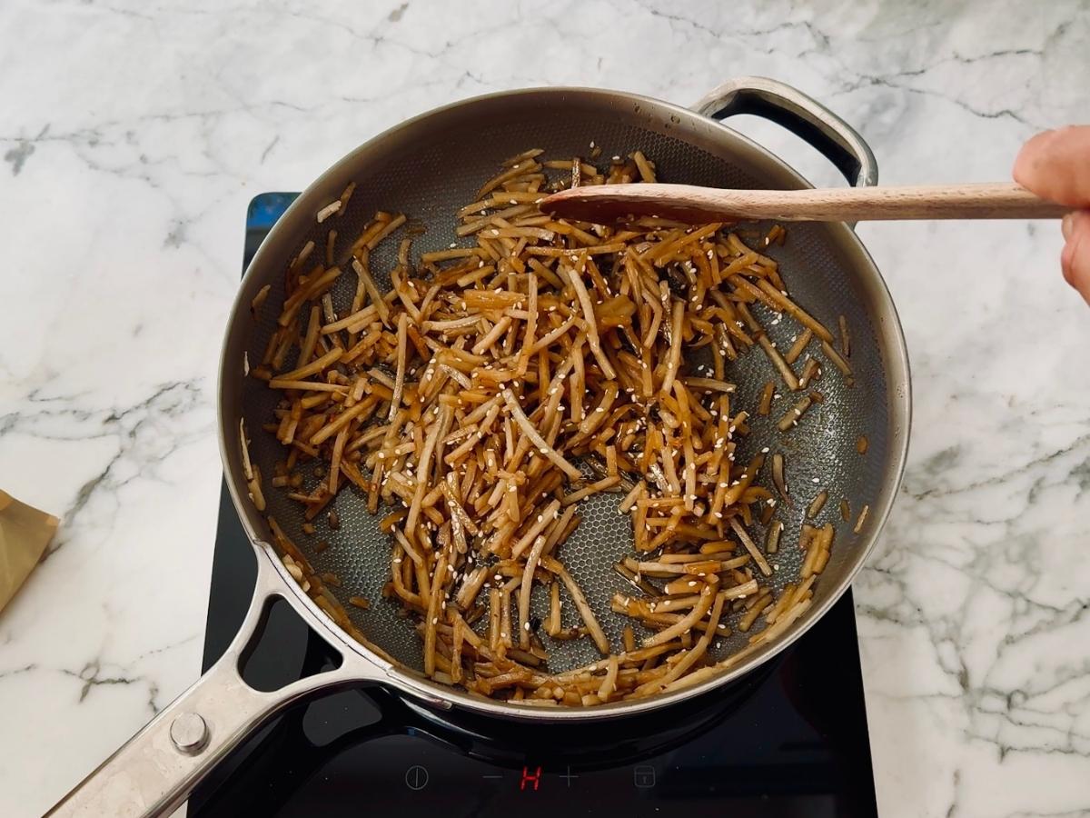 Mirin, soy sauce, sugar, dashi powder, chili flakes, and sesame seeds added to burdock root in pan