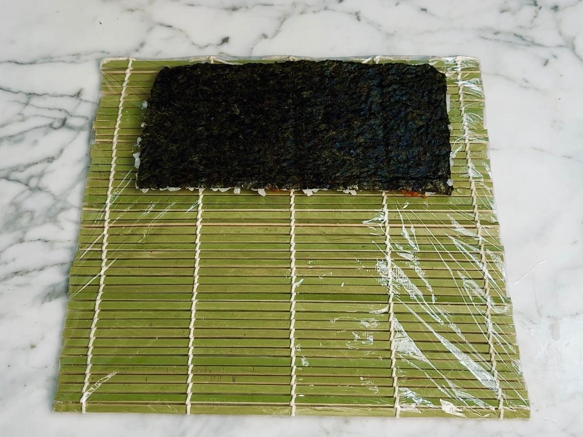 Sushi sheet flipped, with nori now on top and rice facing down on the mat.