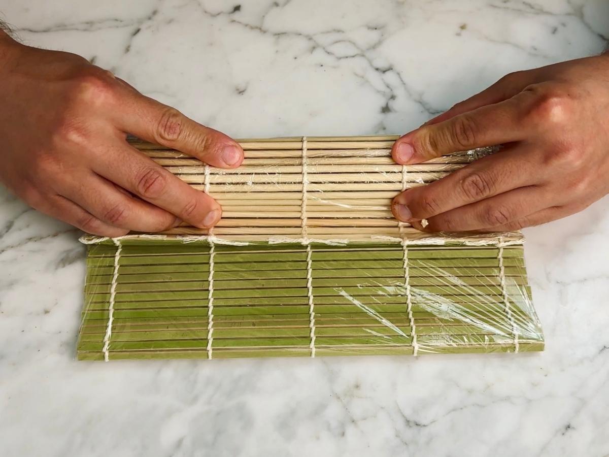 Fully rolled sushi being shaped into a cylinder on the bamboo mat.