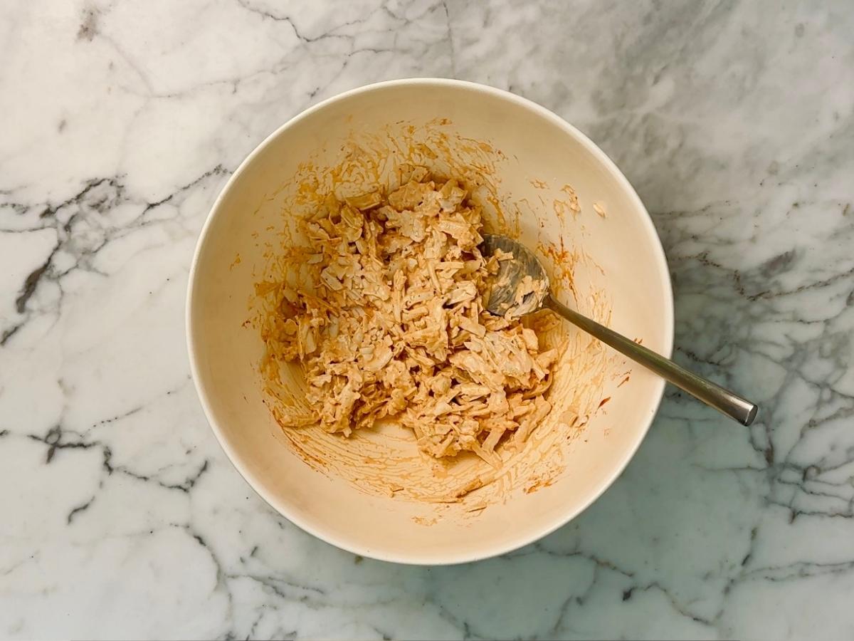 Orange-tinged tofu mixture being stirred with a spoon in a mixing bowl.
