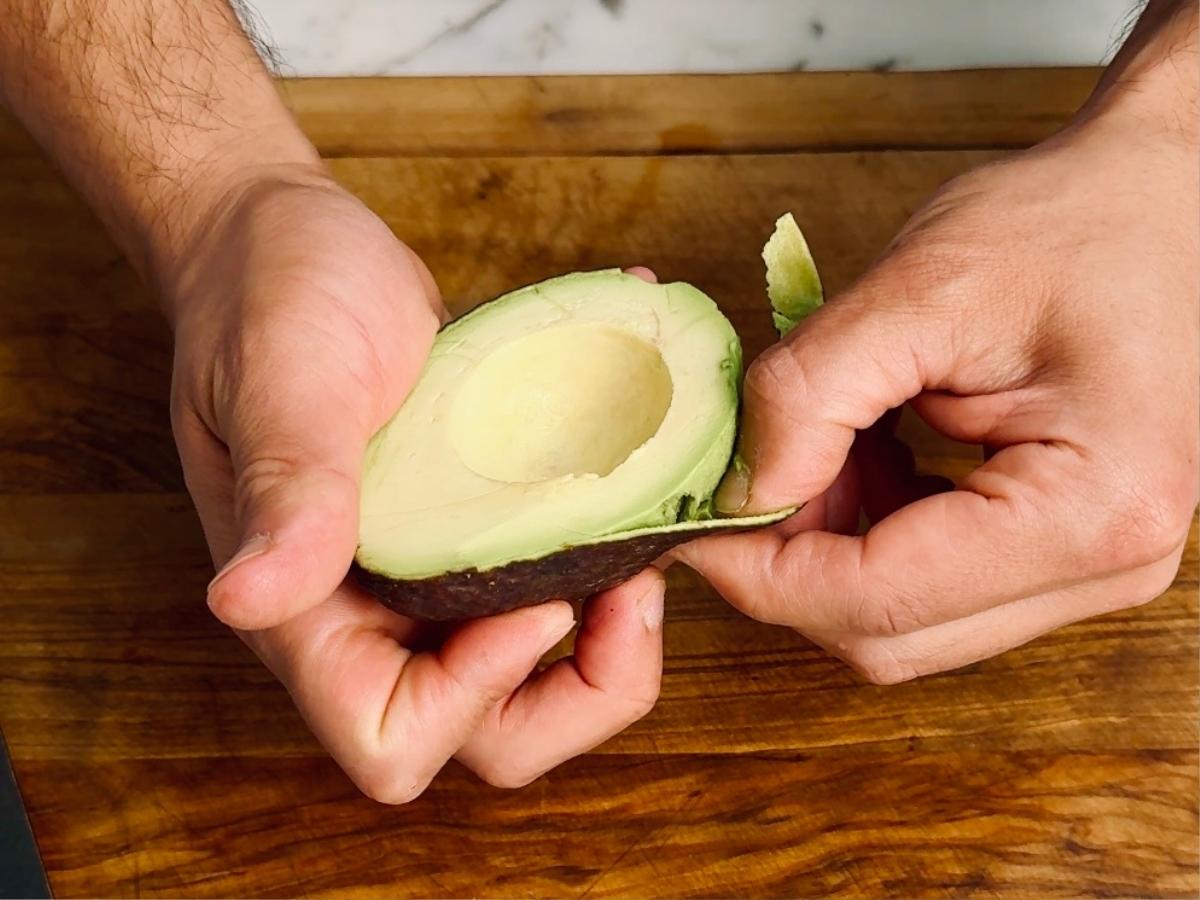 Avocado half with pit removed and skin peeled, resting on a board.